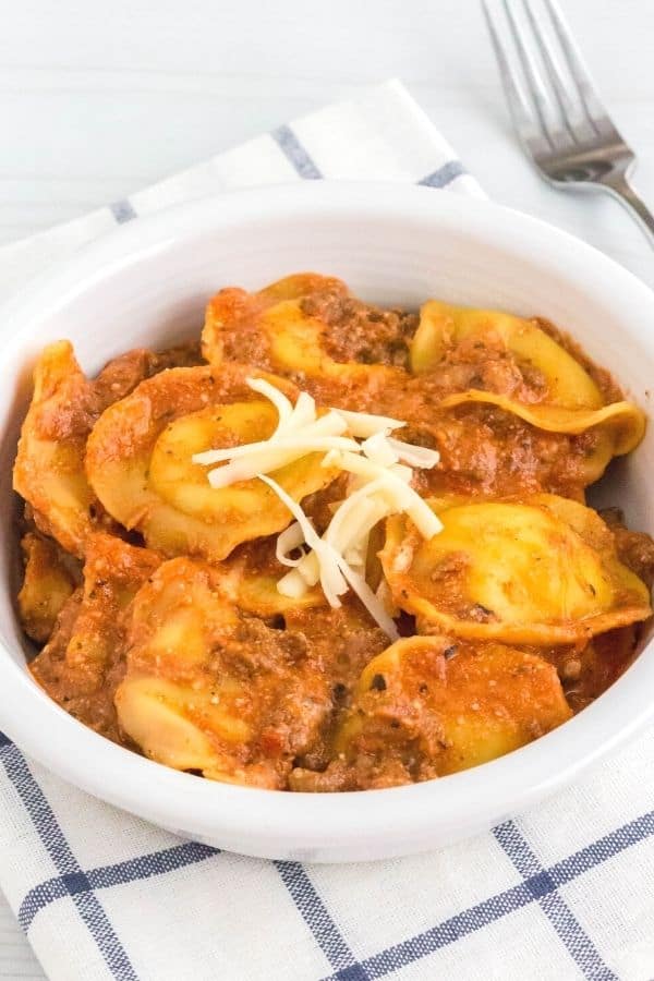 a serving of lazy lasagna made in the Instant Pot with frozen ravioli, complete with meat sauce, ricotta cheese, and a sprinkling of shredded mozzarella, served in a white bowl.