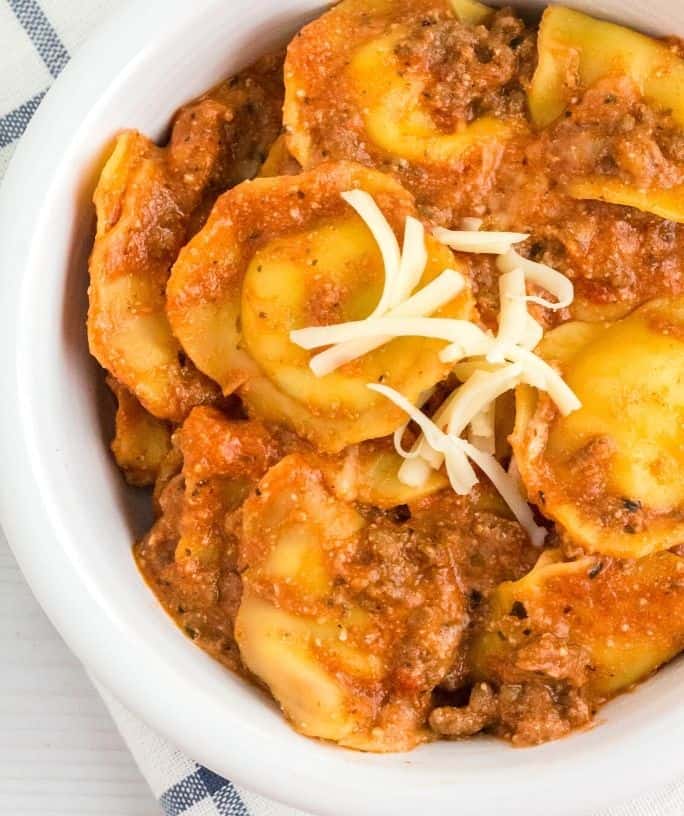 close-up view of Instant Pot ravioli lasagna in a white bowl, with shreds of mozzarella on top.