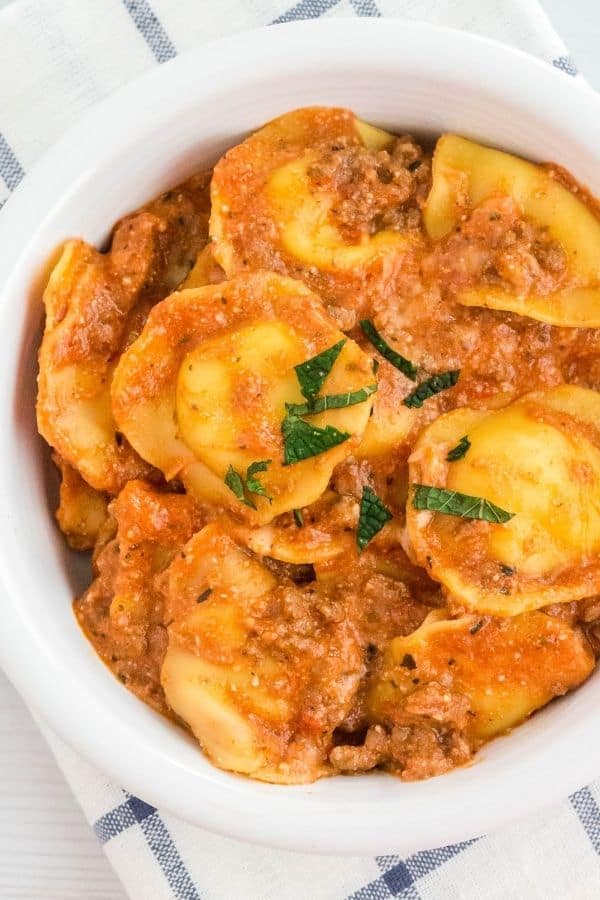 Instant Pot frozen ravioli with meat sauce served in a white bowl, topped with fresh basil.