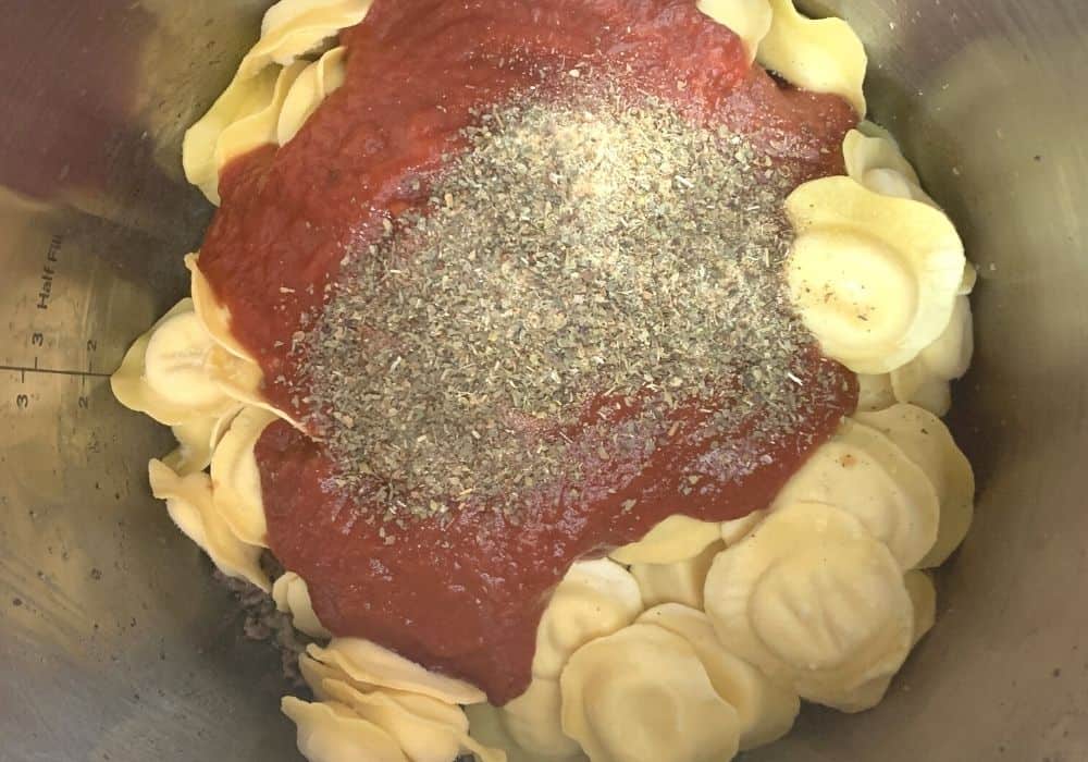 frozen ravioli, spaghetti sauce, and spices layered over the cooked ground beef in the Instant Pot for making pressure cooker ravioli lasagna