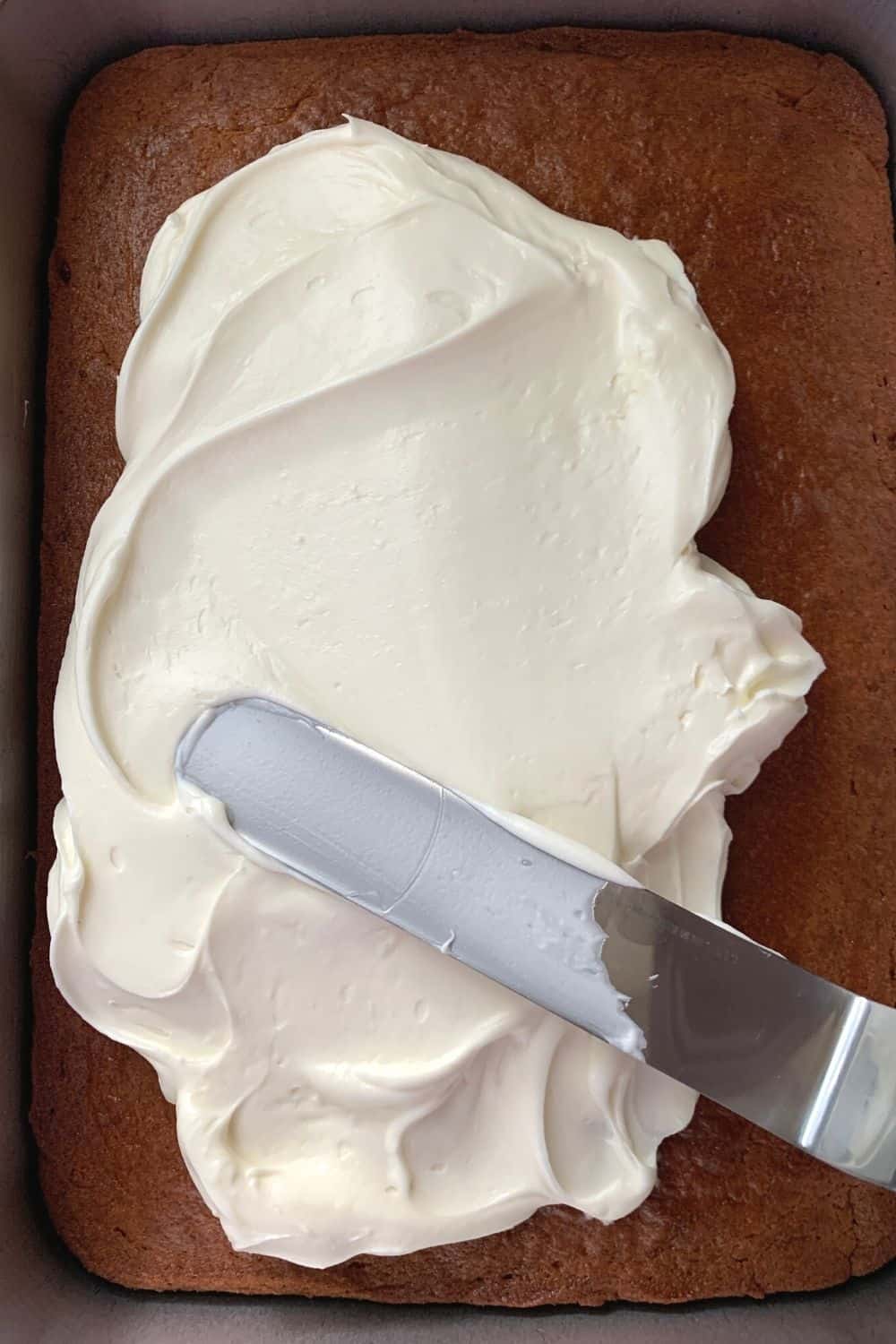 an offset spatula spreading fluffy cream cheese frosting on a baked tomato soup cake