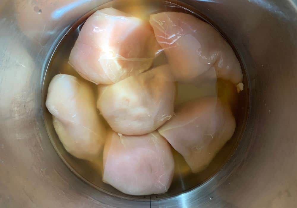 halved chicken breasts in chicken broth in the insert pot of the Instant Pot