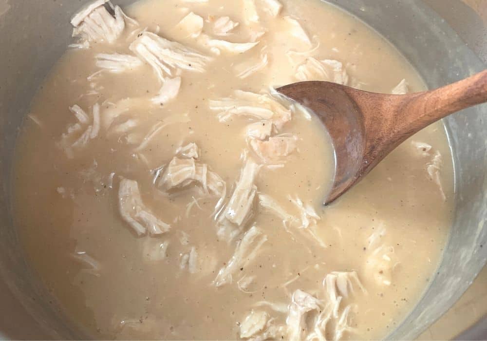 shredded chicken in gravy in the Instant Pot, with a wooden spoon for serving