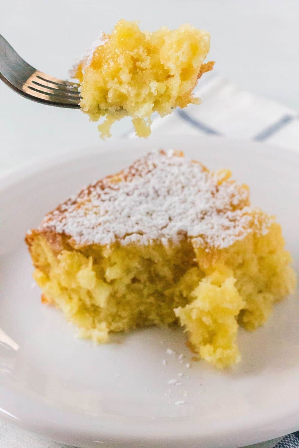 a fork removing a bite of pineapple cake from the serving on a plate
