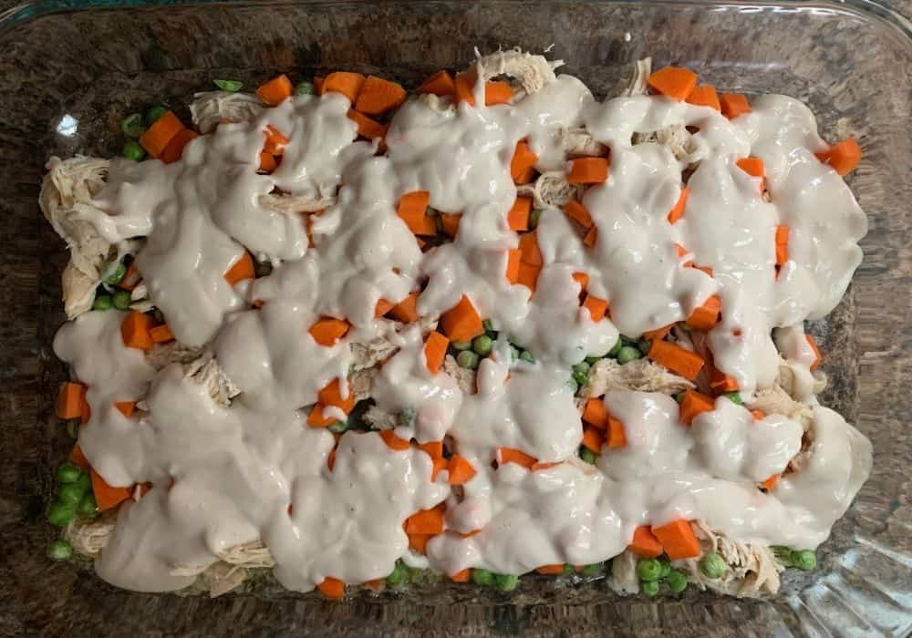 dumpling batter poured over the chicken, peas, and carrots in a baking dish