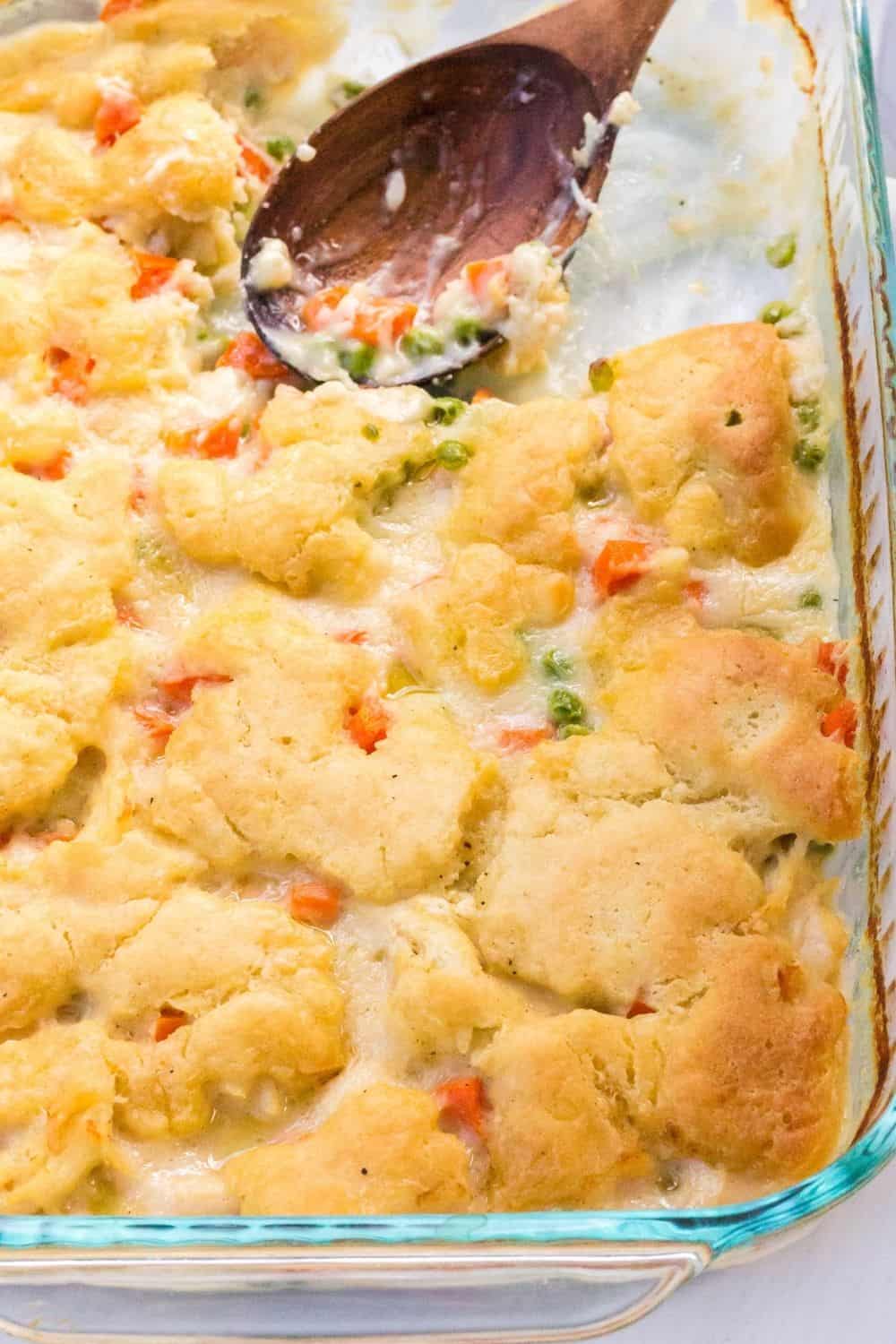 a pan of baked chicken and dumplings casserole, with a wooden serving spoon next to an area where some of the casserole has been scooped out