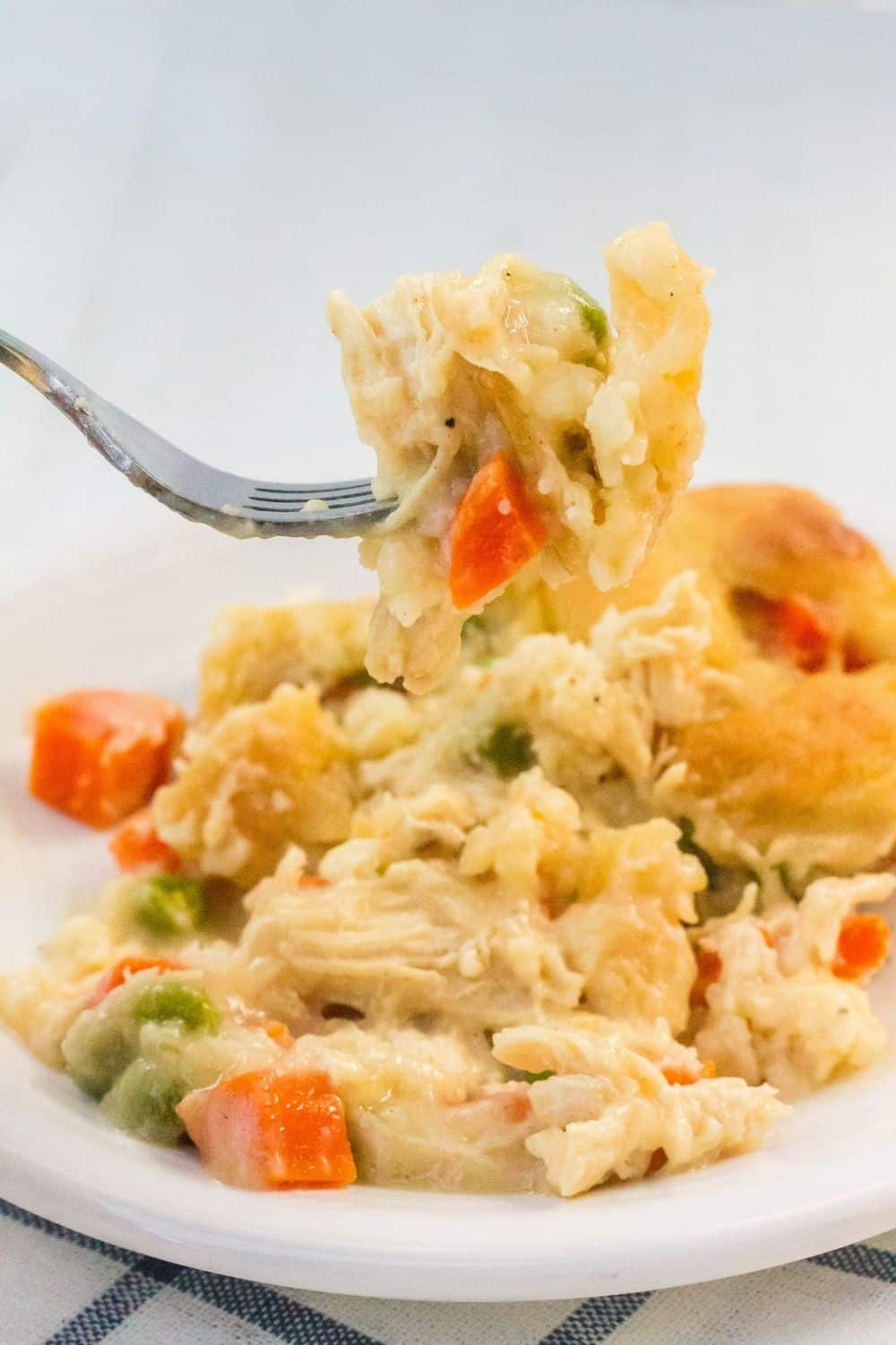 a fork lifting a bite of chicken and dumplings cooked in the oven from a white serving plate