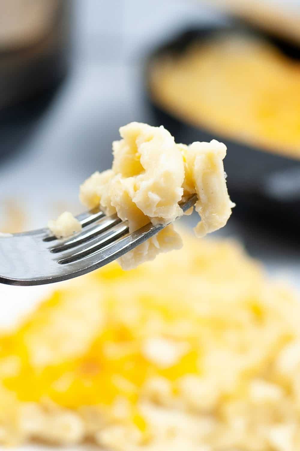 a fork lifting a bite of baked macaroni and cheese from the serving plate