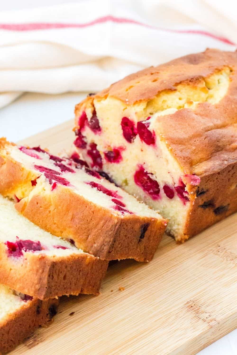 cream cheese cranberry bread loaf on a cutting board, partially sliced for serving