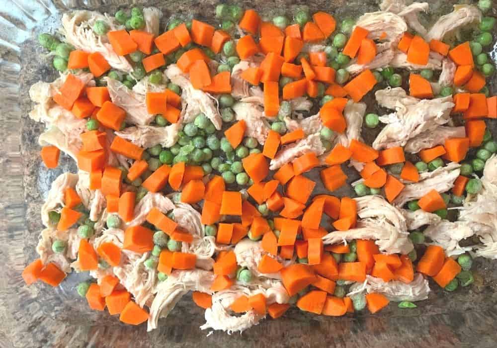 chicken, carrots, and peas on top of melted butter in a baking dish