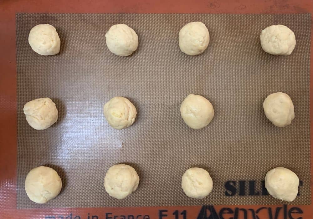 round balls of pineapple cookie dough on a silicone mat on a baking sheet 