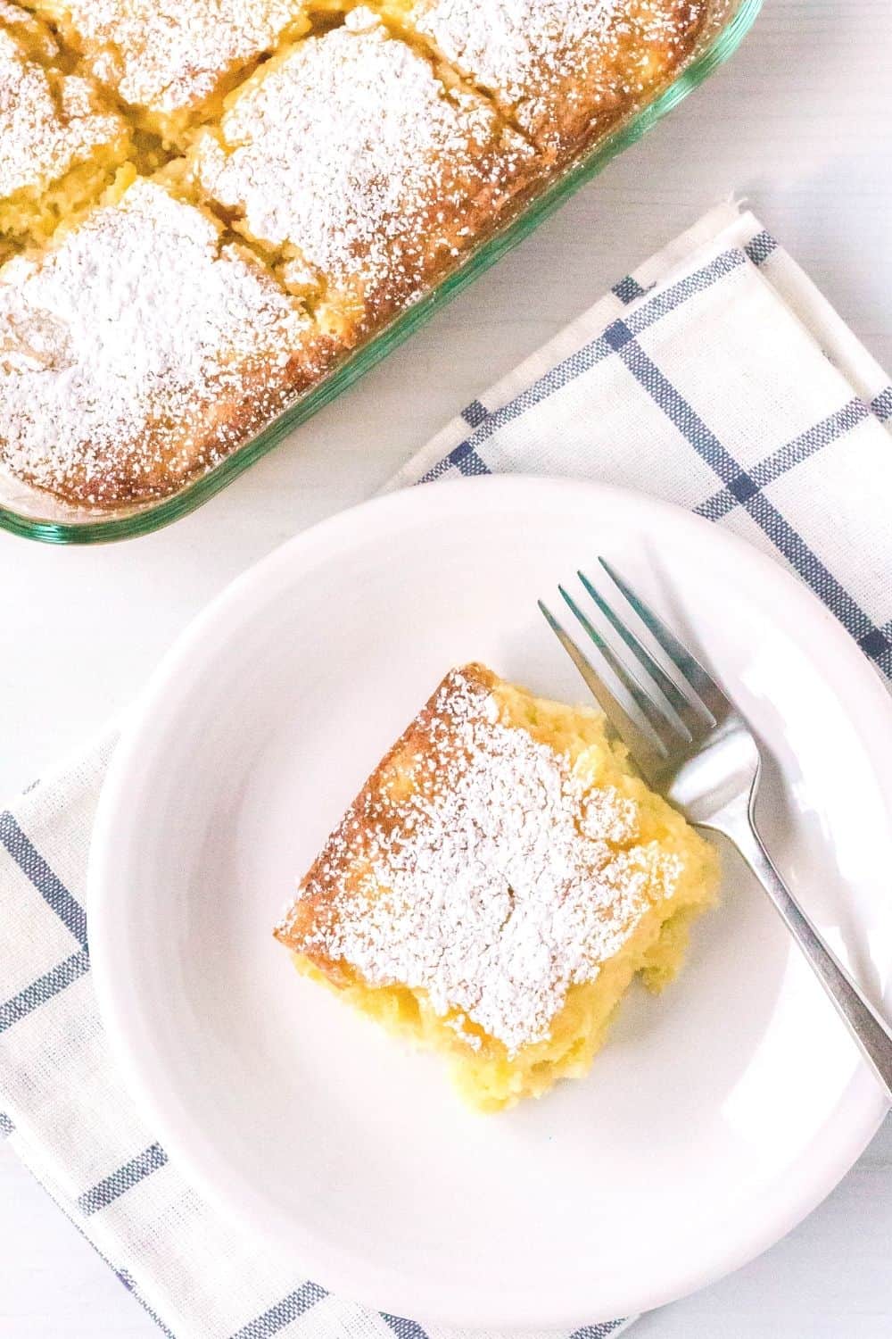 slice of pineapple cake on a white plate with a fork, with the remaining pan of cake in the background