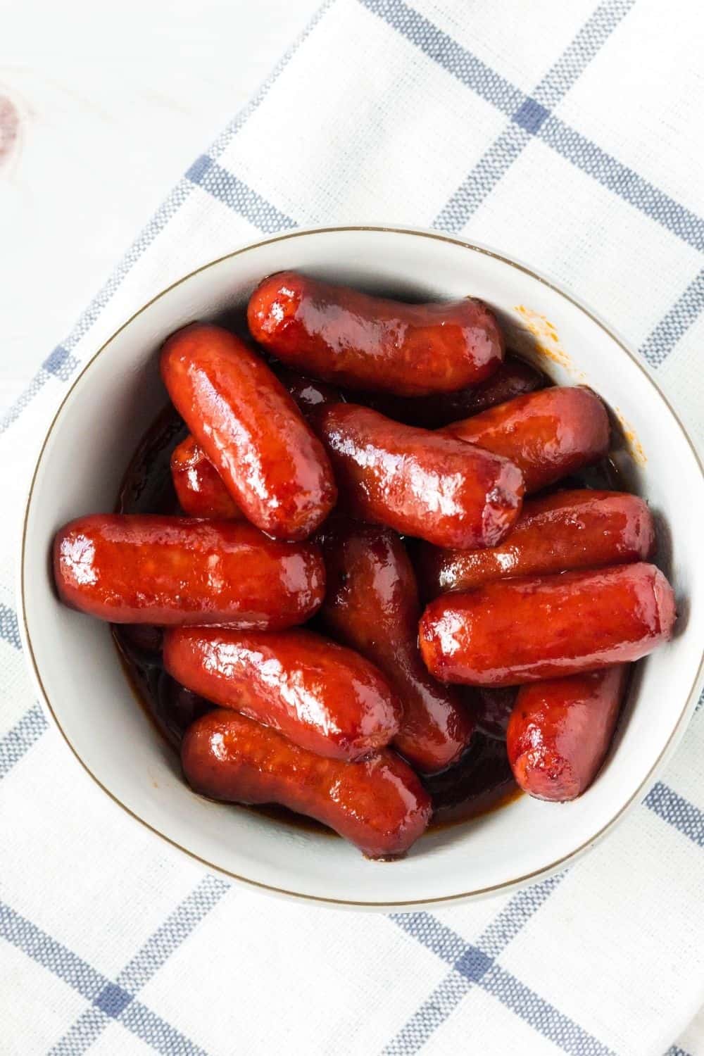 Instant Pot little smokies in bbq grape jelly sauce, served in a white bowl atop a blue and white checked napkin
