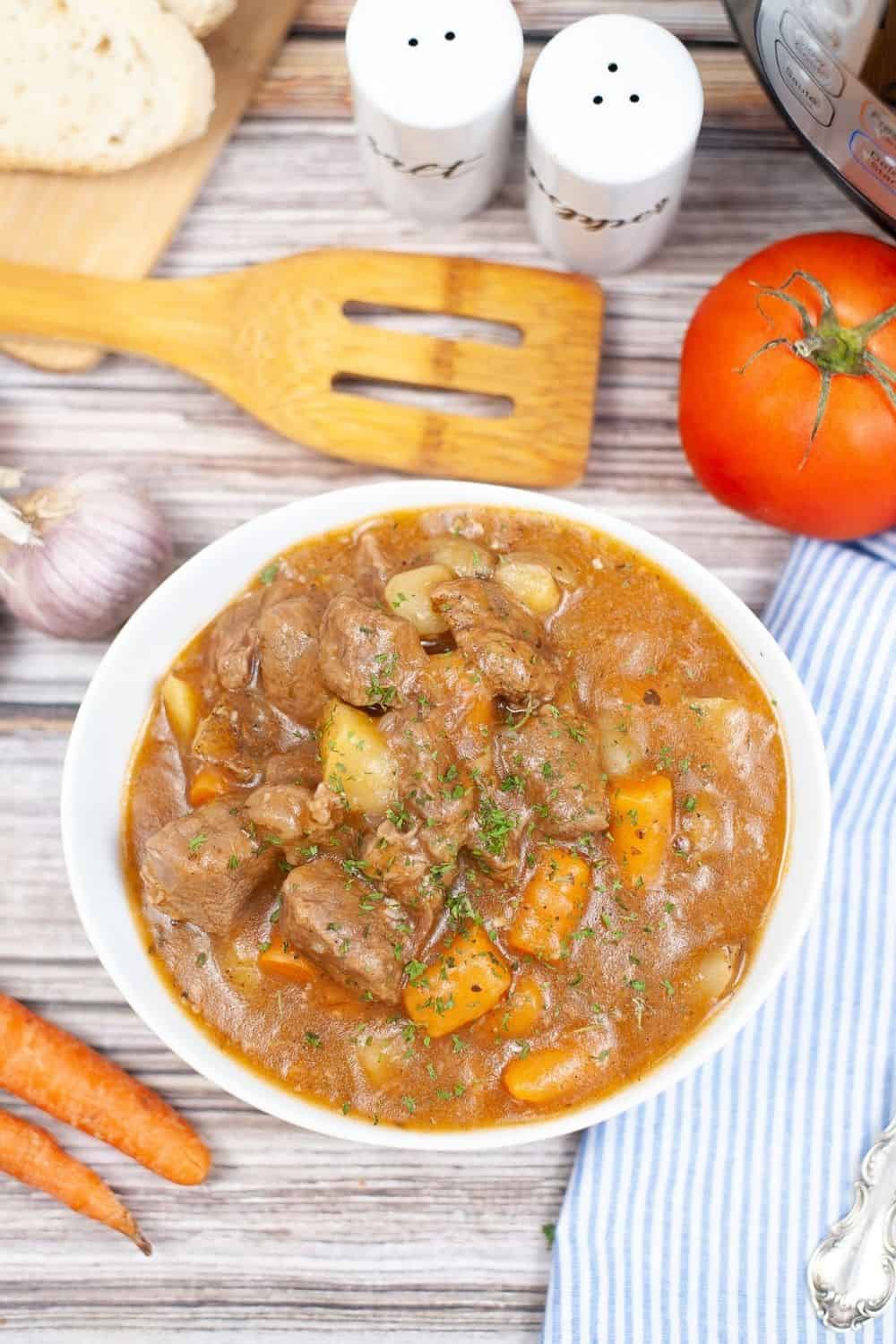 Instant Pot pressure cooker beef stew served in a white bowl, with the pressure cooker and utensils in the background