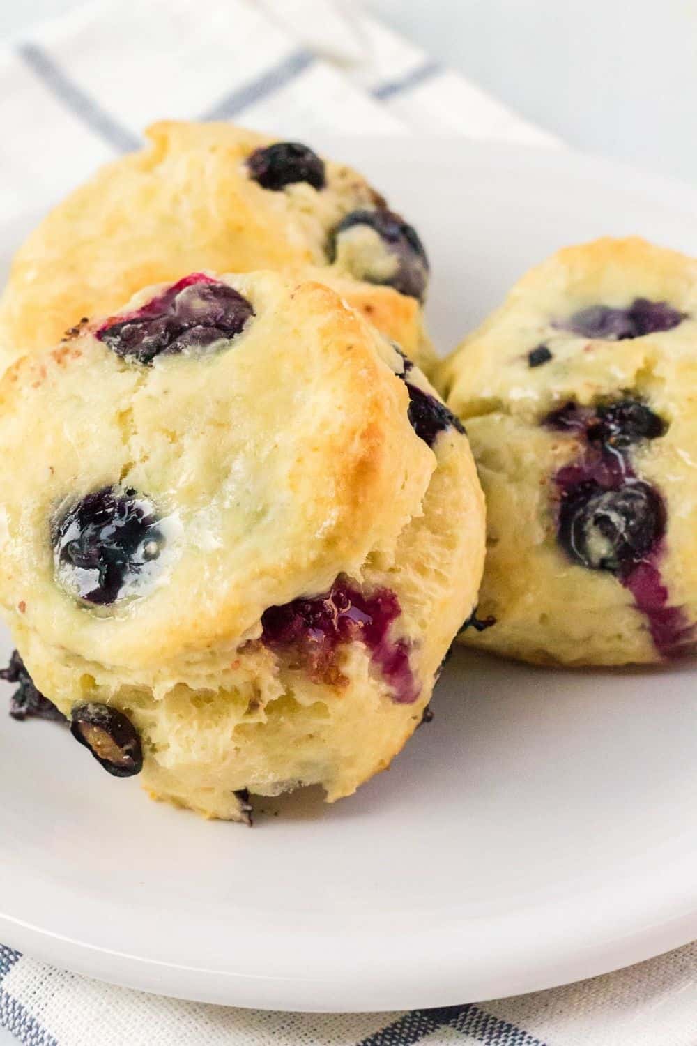 three freshly baked glazed blueberry biscuits on a white plate