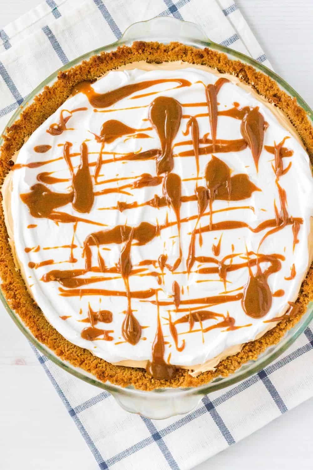 overhead view of a whole caramel cream pie topped with cool whip and a drizzle of dulce de leche