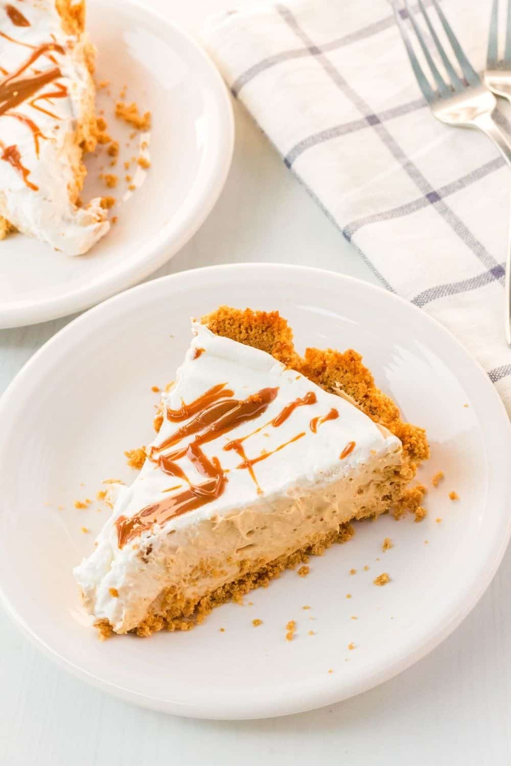 two slices of caramel cream pie on white plates for serving, with two forks in the background