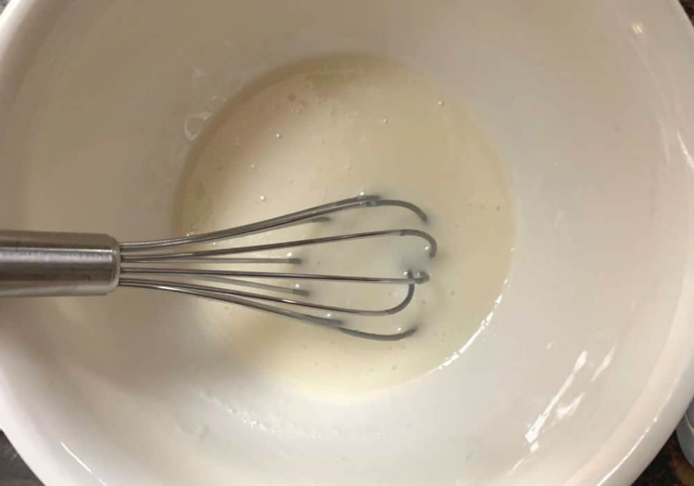 a whisk in a small bowl of icing for glazing the blueberry biscuits after they're baked
