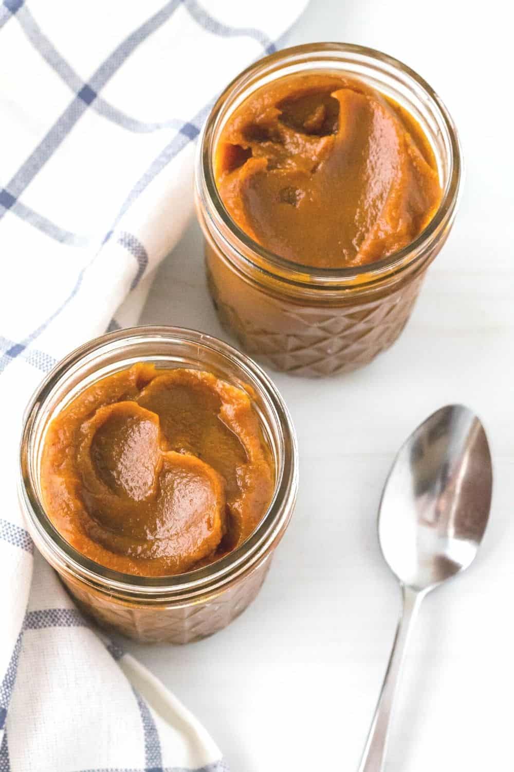 two jars of pumpkin butter with a spoon next to them