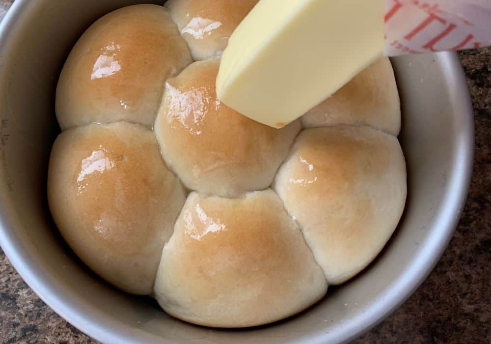 A stick of butter is rubbed across the tops of hot Rhodes rolls, melting onto the surface