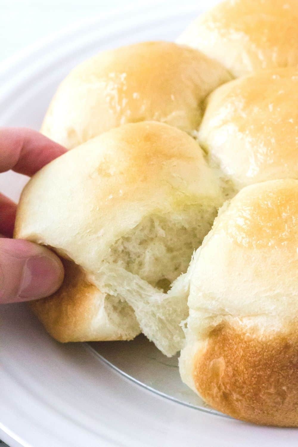 A woman's hand pulls apart a frozen Rhodes dinner roll that was risen in the Instant Pot and baked in the oven.