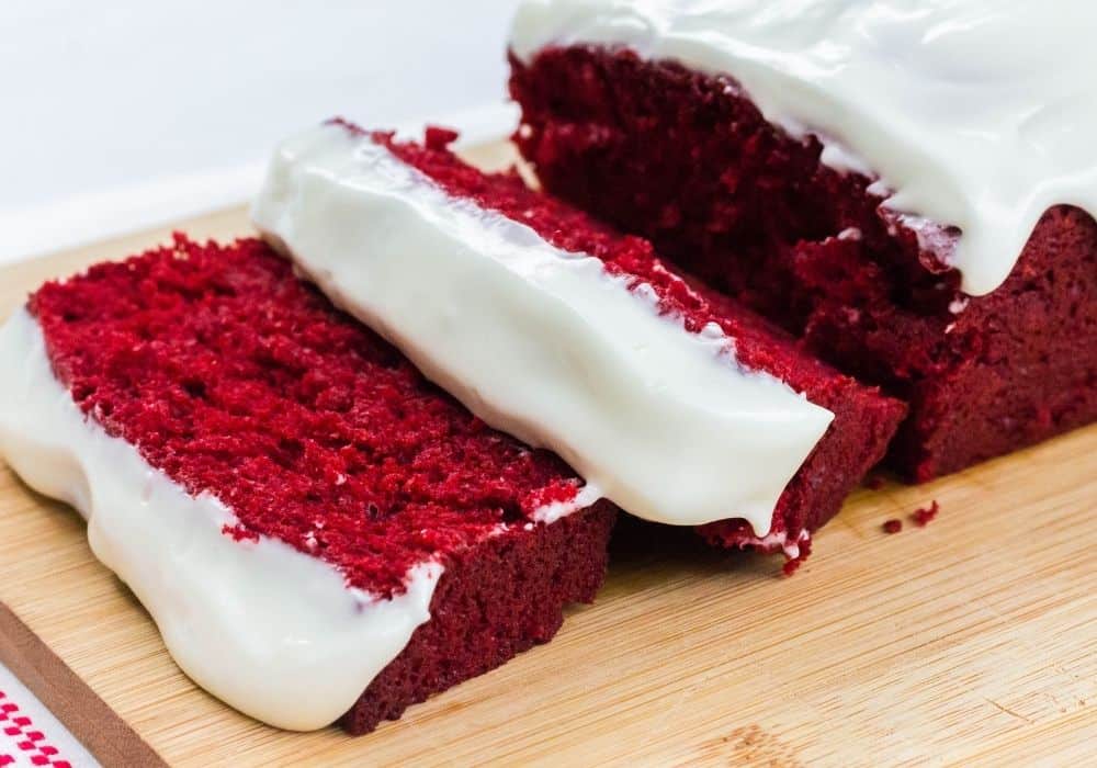 slices of red velvet bread, topped with cream cheese icing glaze, on a wooden cutting board