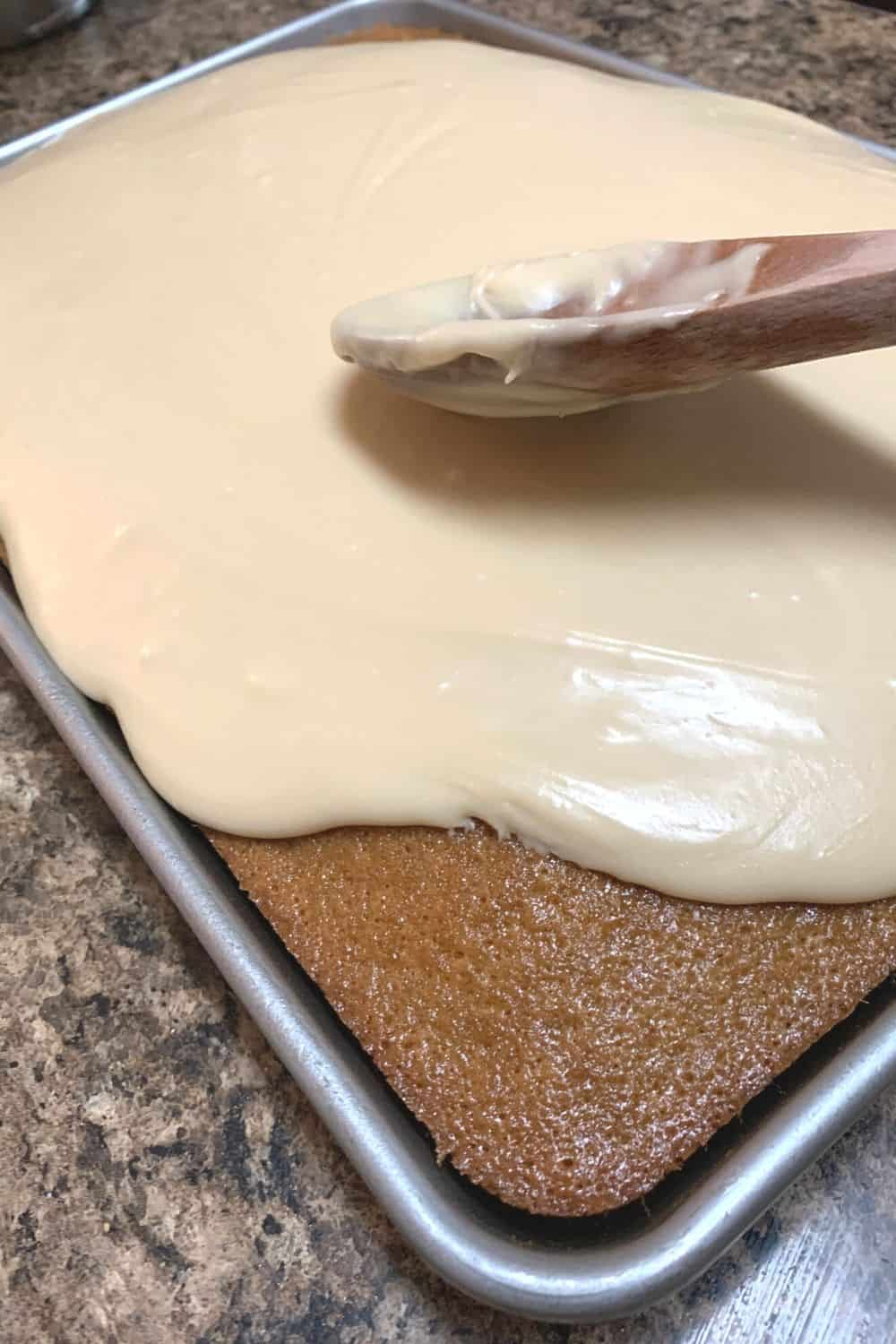 caramel brown sugar frosting being spooned over the baked buttermilk sheet cake