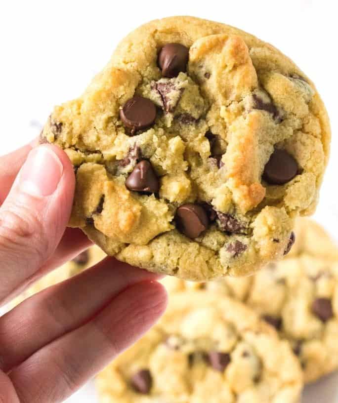 a woman's hand holds a chocolate chip cookie made with no brown sugar