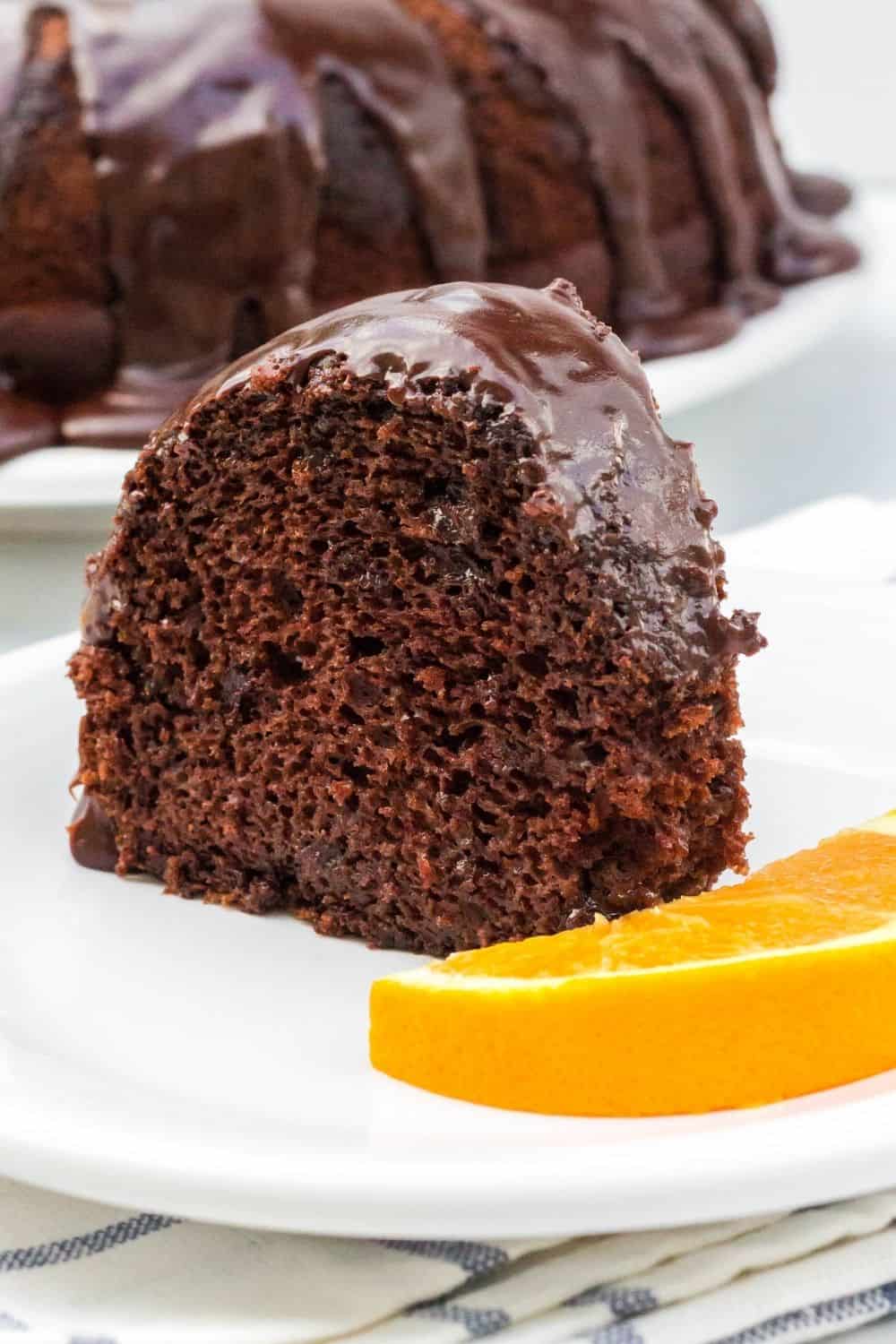 Slice of orange chocolate bundt cake served on a white plate with a garnish of sliced orange