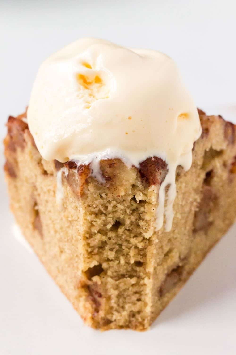 front view of a slice of apple cake with a bite taken out of it, topped with a scoop of melting vanilla ice cream