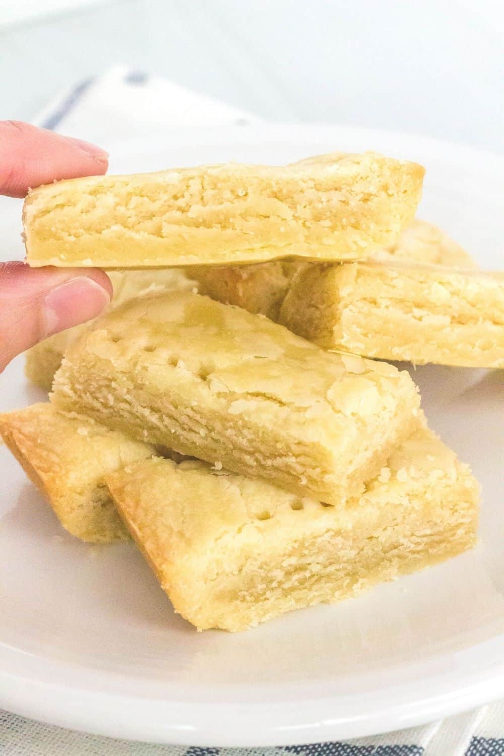 a woman's fingers lift a scottish shortbread cookie from a pile of cookies served on a white plate