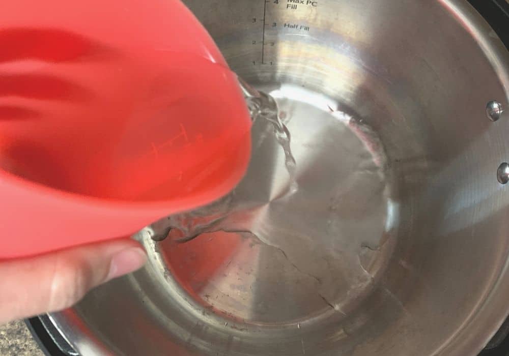 a red measuring cup pours water into the insert pot of the Instant Pot for making apple crisp