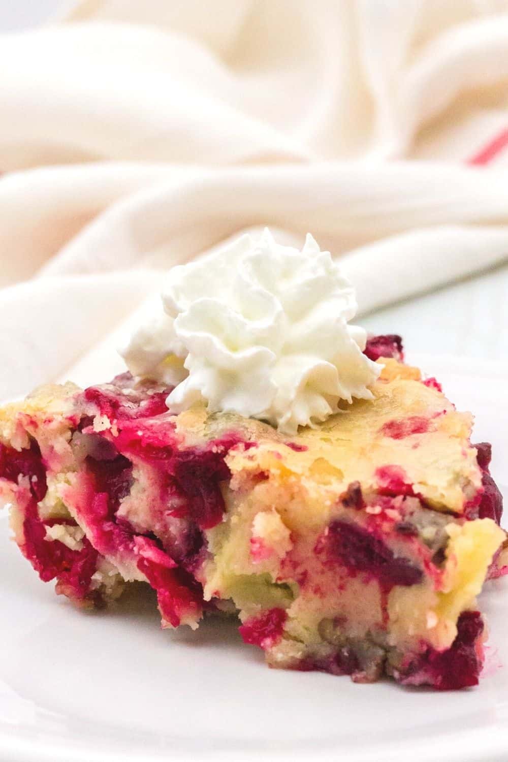 slice of Nantucket cranberry pie served with a dollop of whipped cream on a white plate