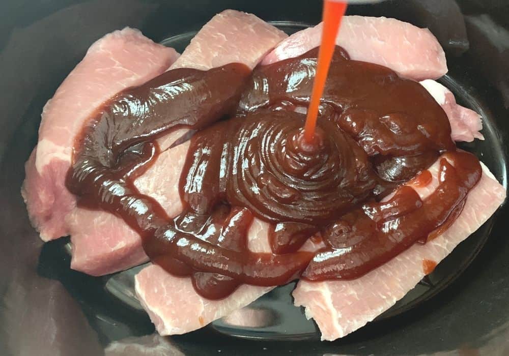 BBQ sauce being poured over raw boneless country style ribs in the slow cooker