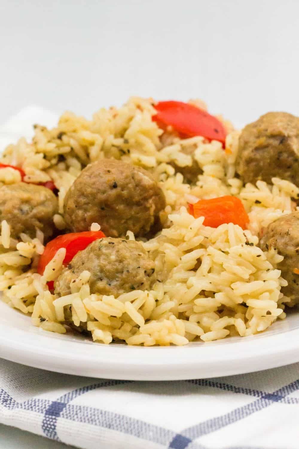 Italian meatballs and rice, along with peppers and carrots, that were cooked in the Instant Pot, served on a white plate atop a blue and white napkin