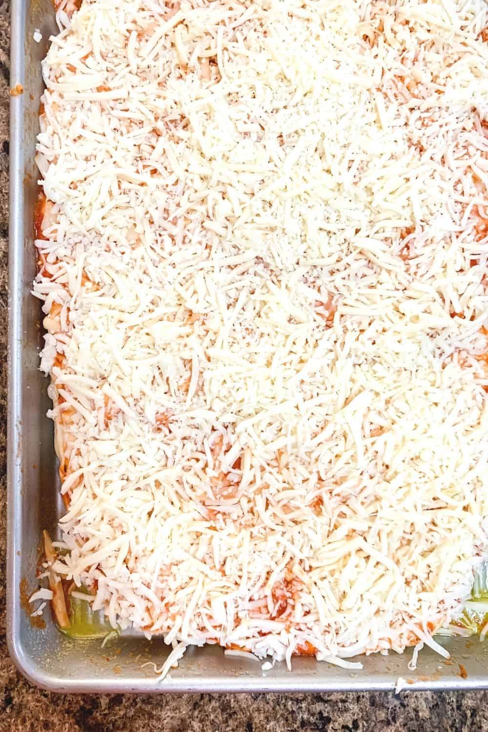 unbaked school pizza topped with sauce and shredded cheese