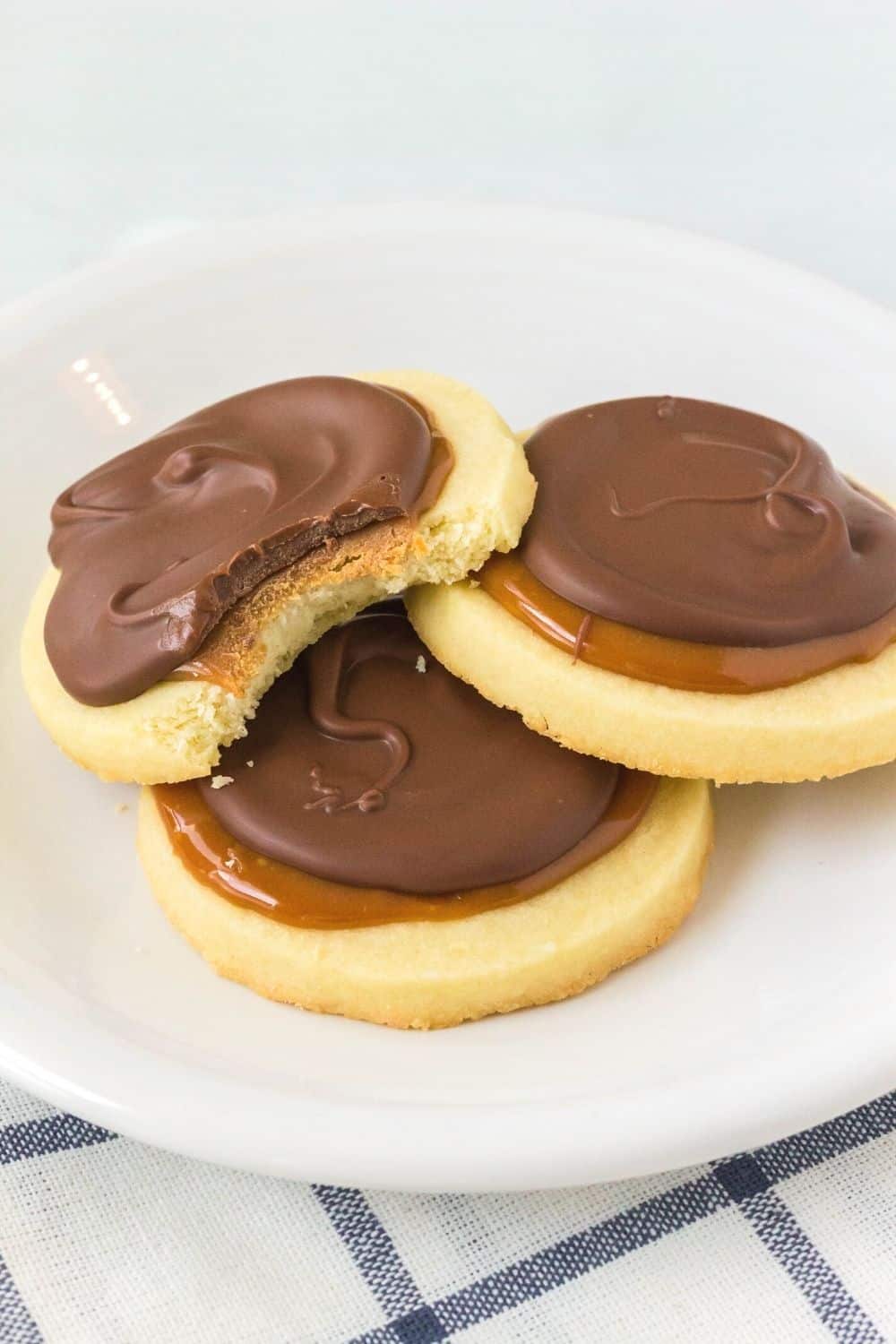 three Twix cookies on a white plate, with a bite taken out of one cookie