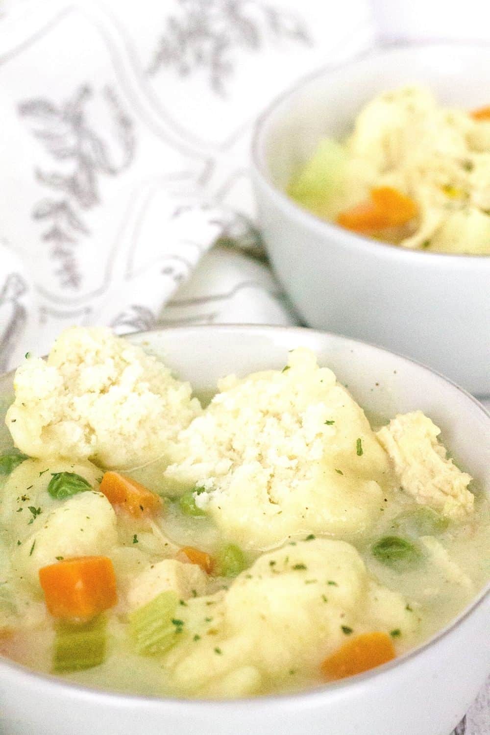 White bowls of chicken and Bisquick dumplings, with a dumpling split in half to show the fluffy interior that demonstrates they are done