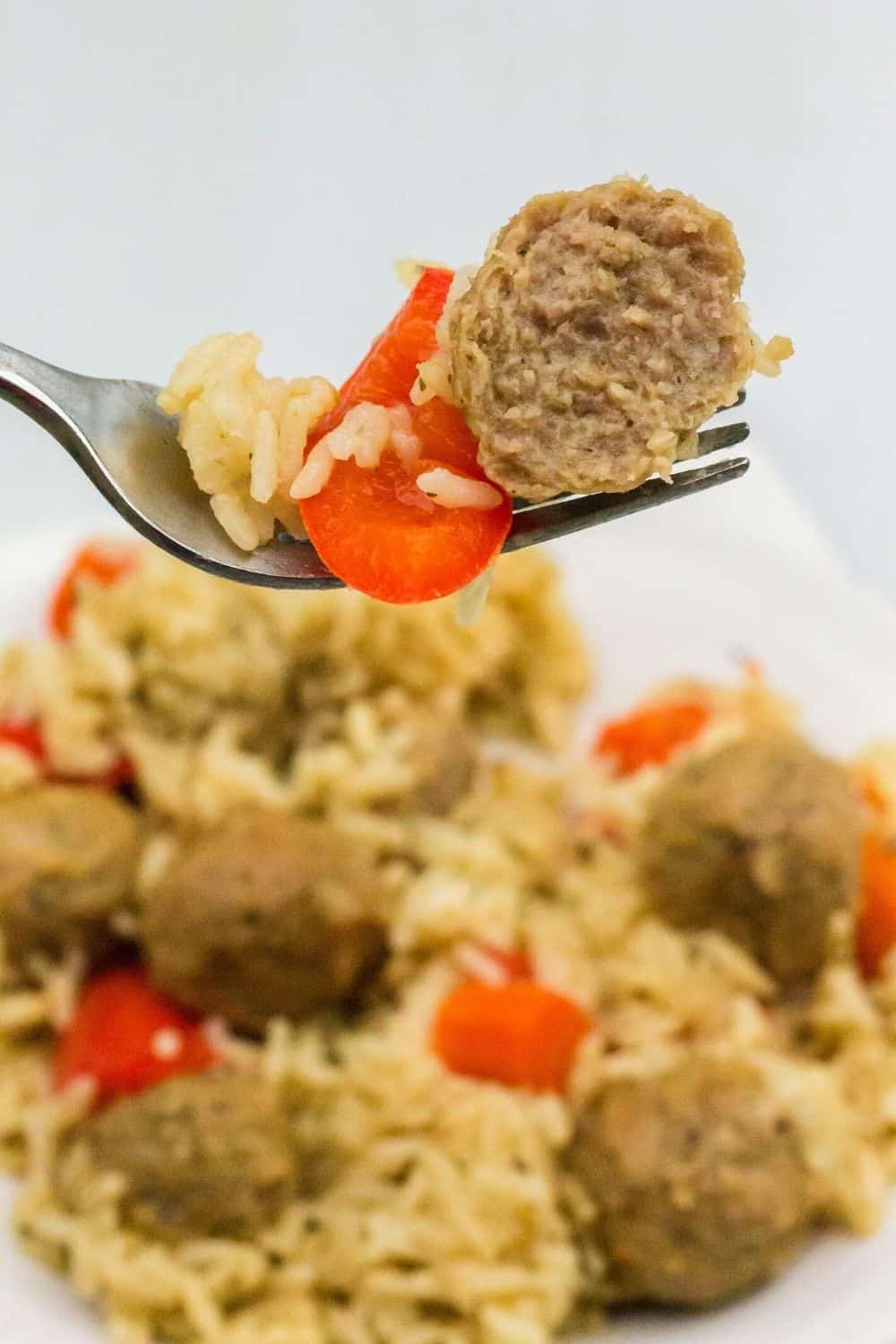 close-up view of a fork holding half a meatball, a pepper, and some rice above the plate of meatballs and rice cooked in the pressure cooker