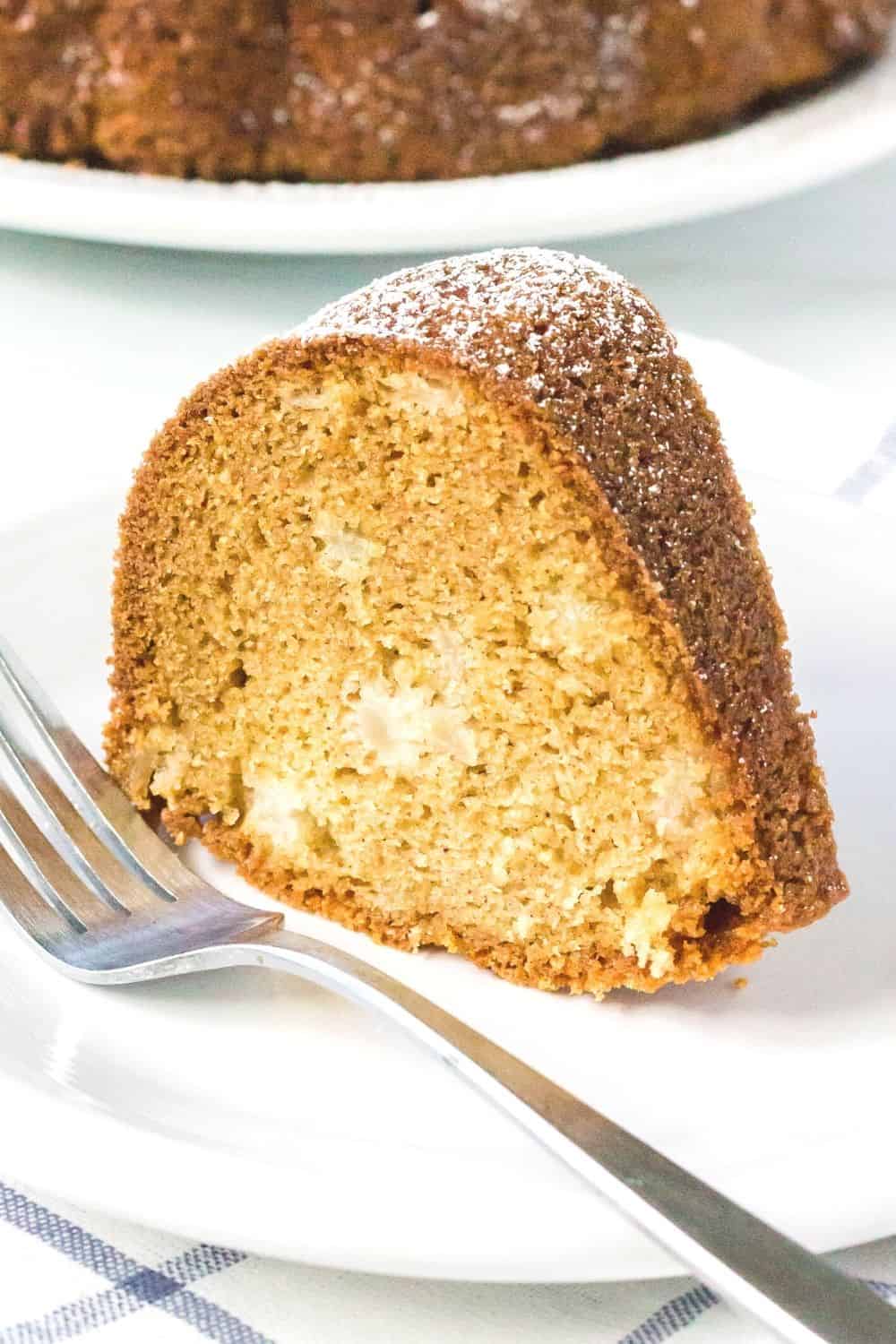 a slice of fresh pear cake standing upright on a white plate with a fork next to it