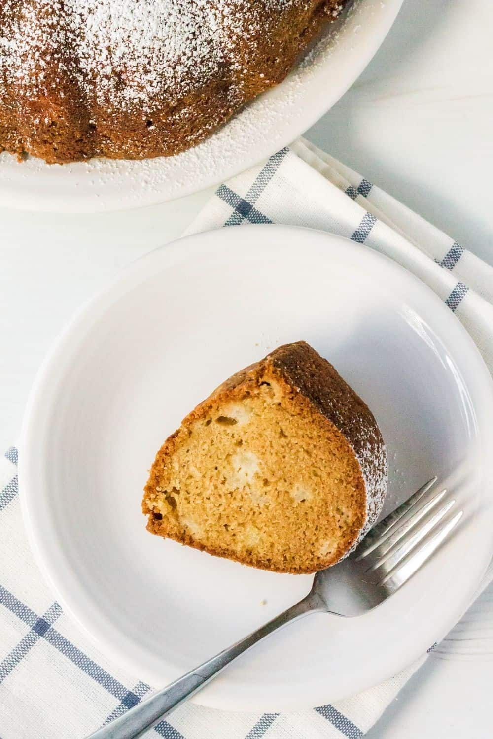 overhead view of a slice of pear cake on a white plate, with the remainder of the cake in the background