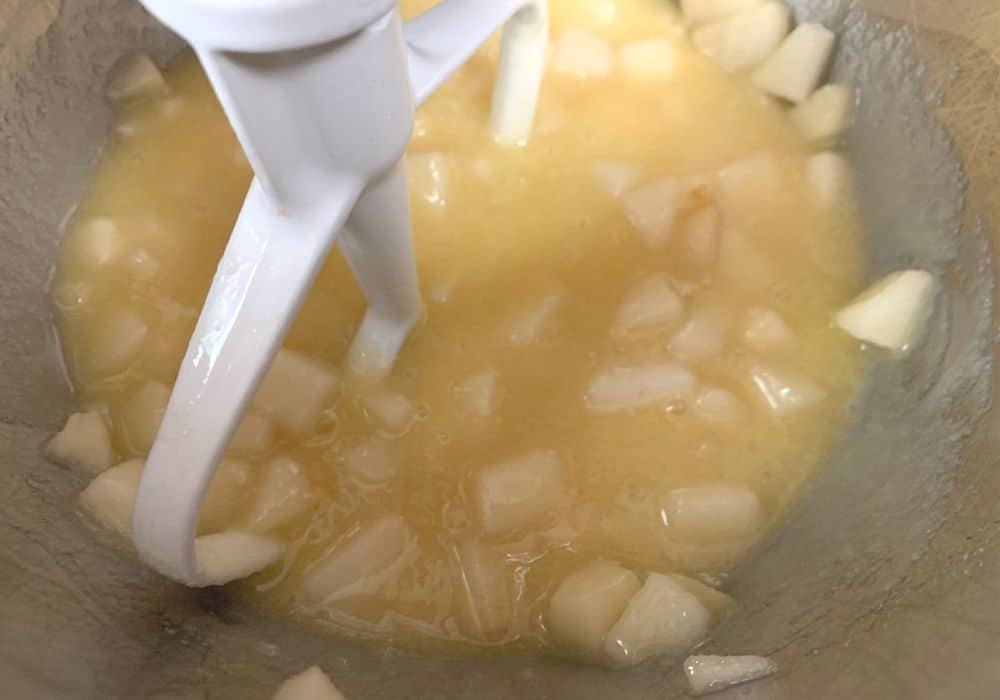vegetable oil, sugar, eggs, vanilla, and pears mixed together in the bowl of a stand mixer