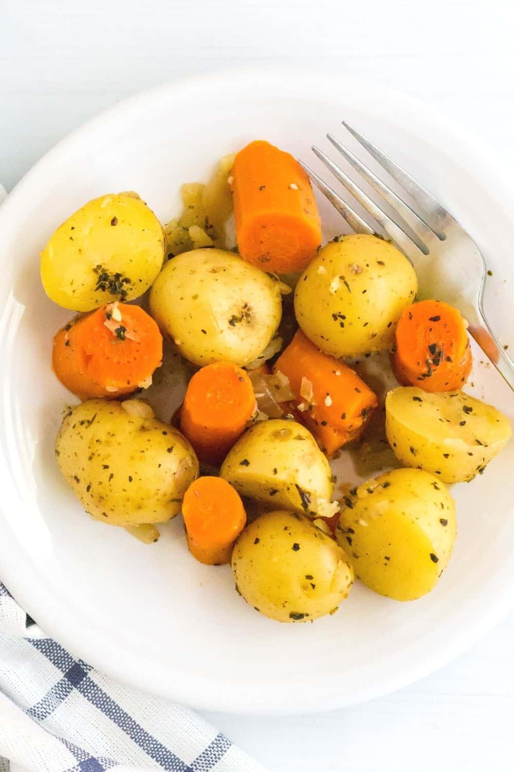 overhead view of a helping of pressure cooker potatoes and carrots on a white plate, with a fork next to the vegetables