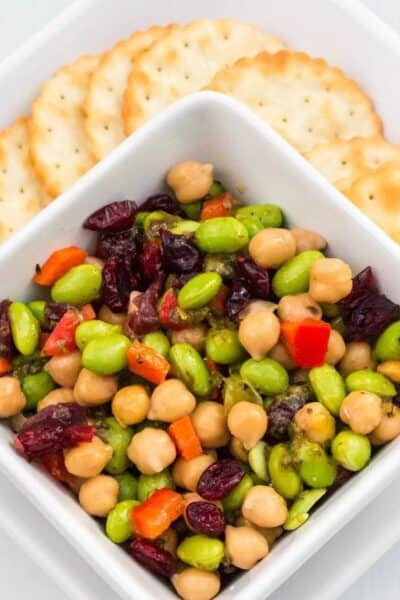 white square bowl serving chickpea and edamame salad alongside crackers