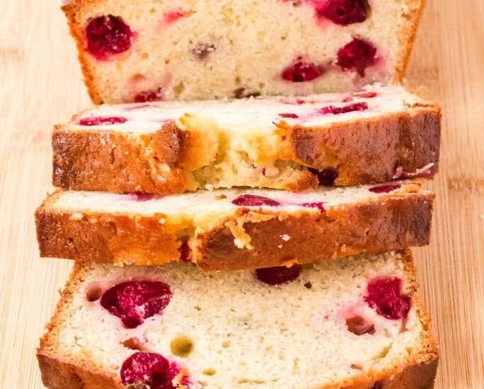 a sliced loaf of cranberry banana bread on a wooden cutting board