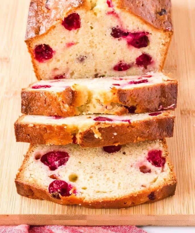 a sliced loaf of cranberry banana bread on a wooden cutting board