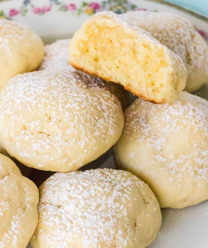 cream cheese cookies on a plate, with one cookie bitten in half