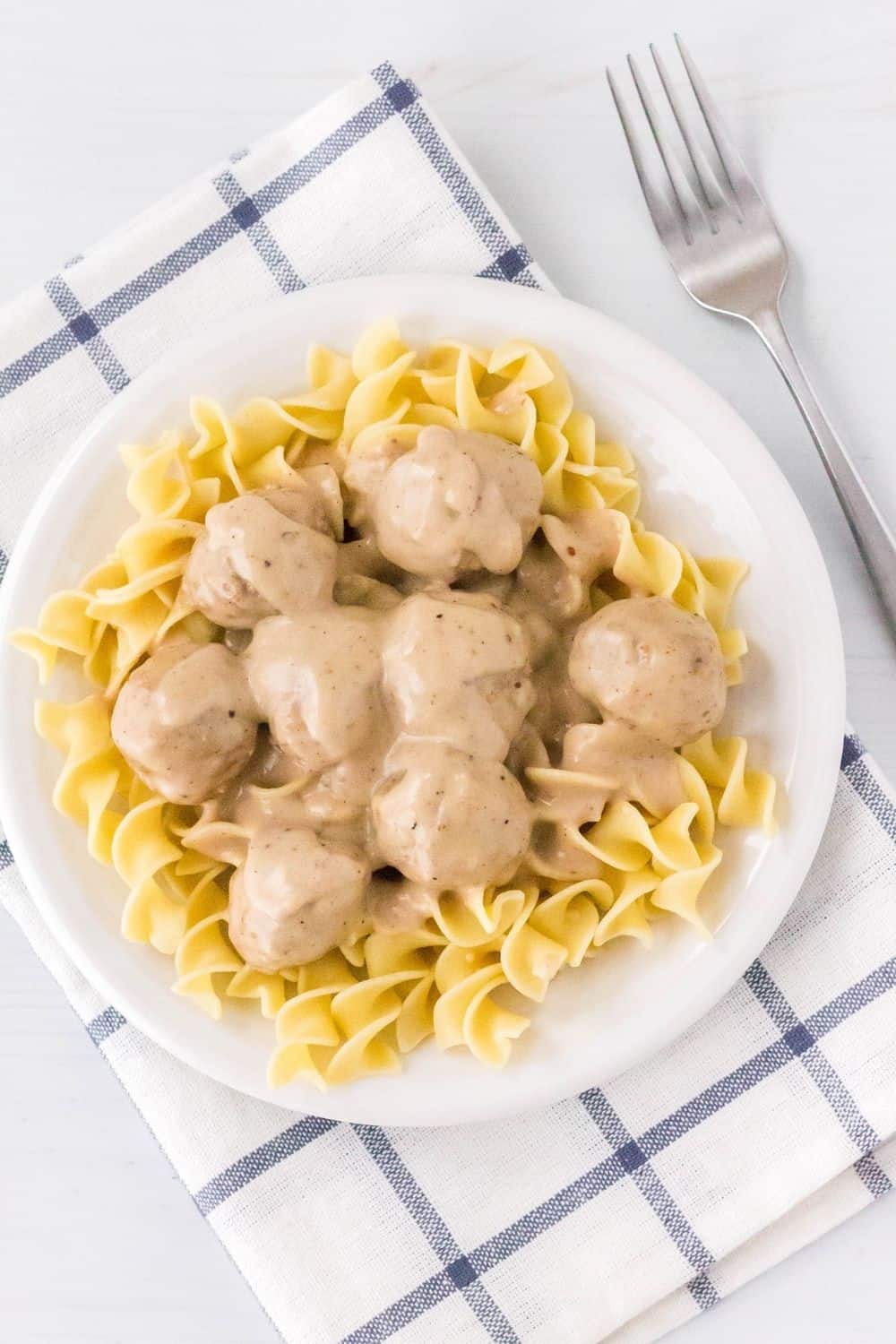 overhead view of a white plate serving egg noodles topped with pressure cooker Swedish meatballs, and a fork off to the side