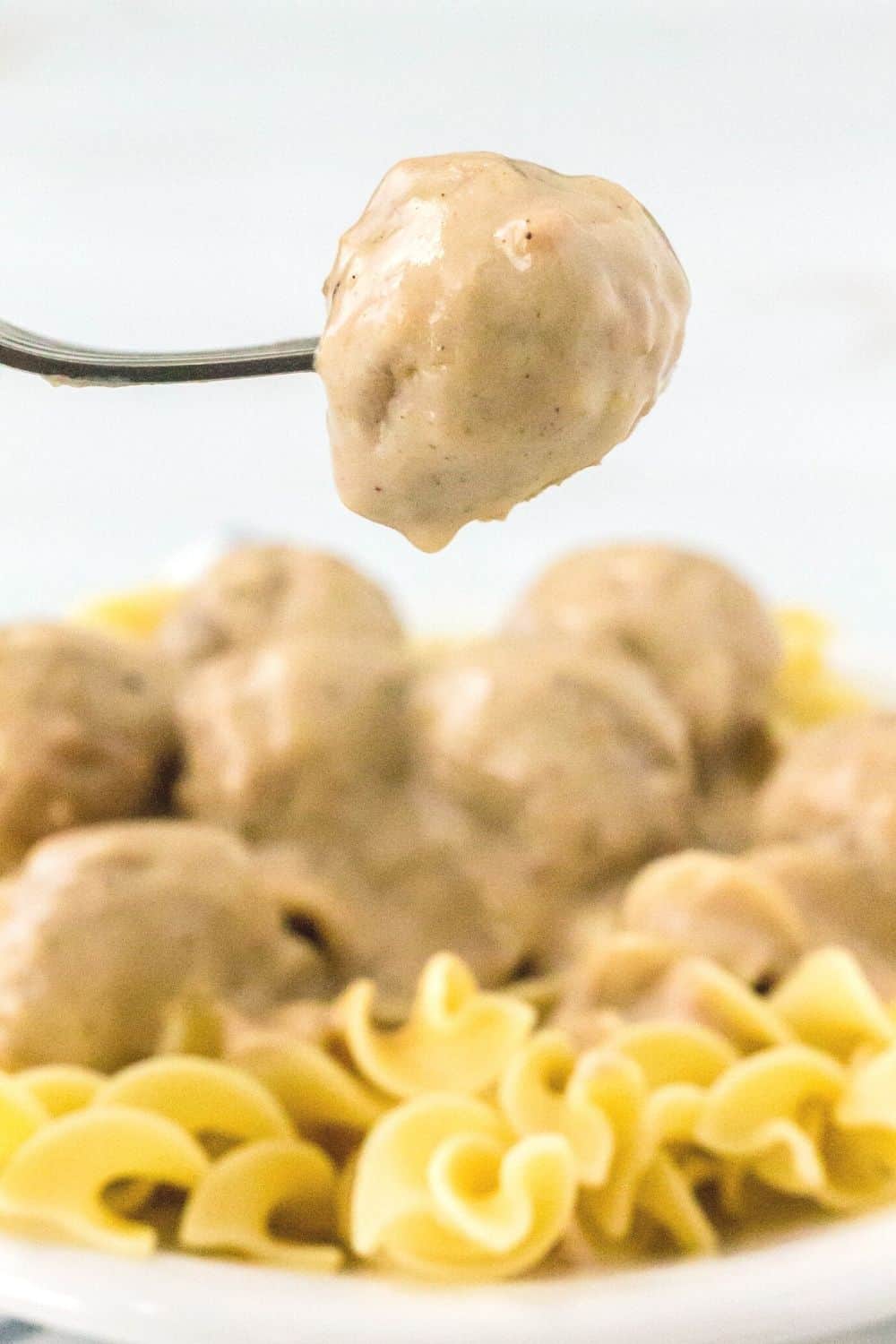 a fork holds a Swedish meatball suspended over a bed of egg noodles and more meatballs that were cooked in the Instant Pot