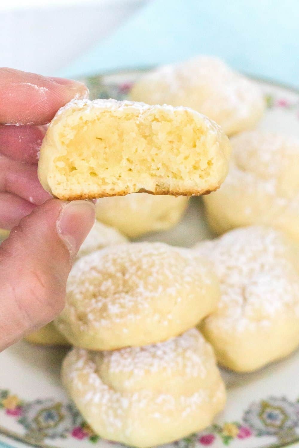 a woman's hand holds half of a cream cheese cookie, showing the delicate interior